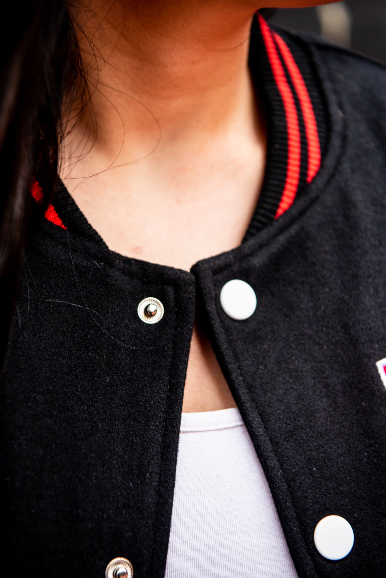 Close-up view of the front collar area of a black RMIT varsity jacket, featuring red trim lines on the collar and white buttons underneath, available at the RMIT Store.